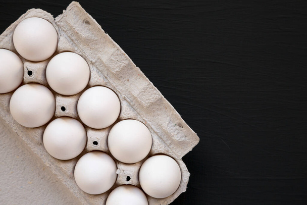 Неприготовленные органические белые яйца в бумажной коробке на черной поверхности, вид сверху. Копирование пространства
. - Фото, изображение