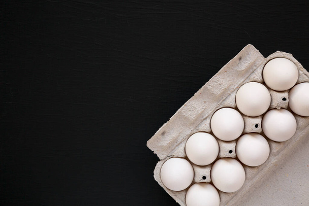 Ungekochte weiße Bio-Eier in einer Pappschachtel auf schwarzer Oberfläche, Ansicht von oben. Flach liegend, über Kopf, von oben. Kopierraum. - Foto, Bild