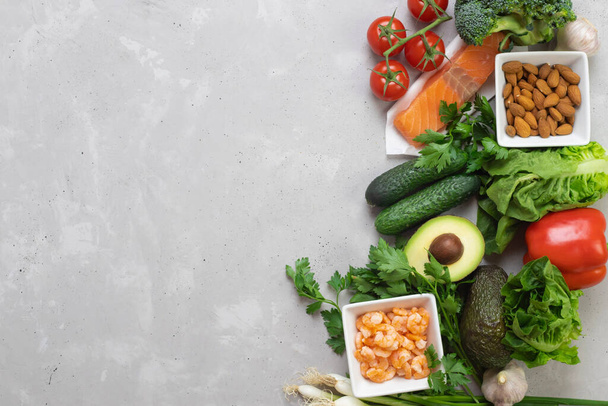 Понятие диетического, сбалансированного питания. Свежие зеленые овощи, красная рыба, орехи и бобовые лежат на сером фоне. Место для текста
 - Фото, изображение