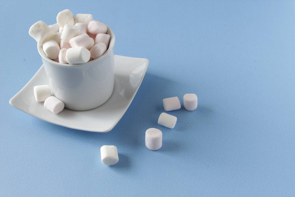 White Fluffy marshmallows in white cup isolated on blue background. Mini marshmallows. Winter food background concept. - Foto, Imagen