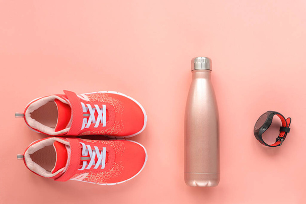 Red sneakers, sport watch and bottle with water on coral pink background. Concept of healthy life, sport and training, top view, copy space. - Photo, Image
