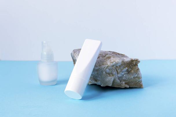 Немаркированная белая сливочная трубка на каменной и стеклянной бутылке сыворотки. Концепция экологически чистых косметических продуктов. Синий фон
 - Фото, изображение
