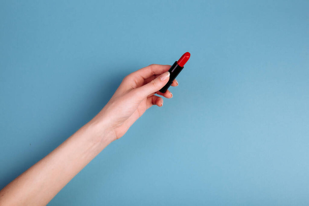 The woman's hand is taking red lipstick. isolated On the blue background. - Φωτογραφία, εικόνα