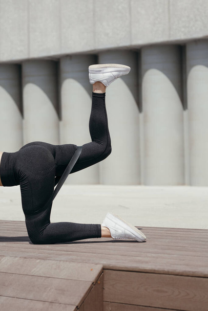 Ženské nohy v černé sportovní punčocháče při provádění gymnastických cvičení s elastickou gumičkou. - Fotografie, Obrázek