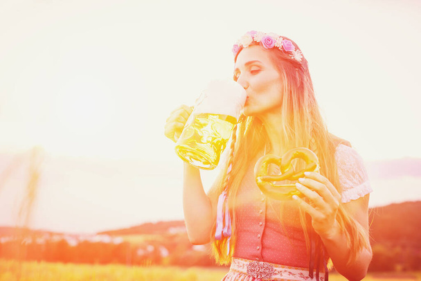 Bavarian woman with beer and pretzel in beautiful landscape - Photo, Image