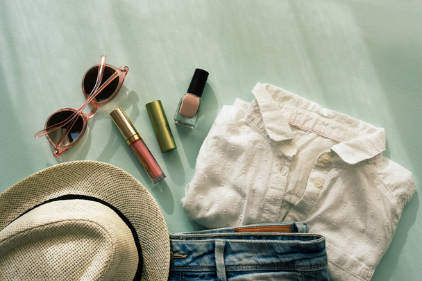Vrouwen zomer mode accessoires, hoed, zonnebril, shorts, t-shirt, cosmetica in het zonlicht met schaduwen. - Foto, afbeelding