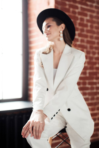 Молодая девушка в белом костюме и черной шляпе. Концепция одежды
. - Фото, изображение