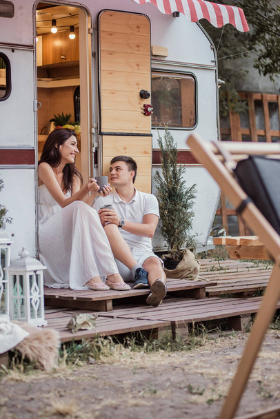A beautiful couple drinks hot drinks for breakfast early in the morning, talking, looking at each other and laughing. The concept of rest in the country in a caravan. Honeymoon for Just Married - Foto, Bild
