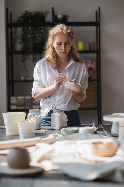 Jovem no estúdio de cerâmica limpando tinta de esmalte desnecessária com uma esponja
. - Foto, Imagem