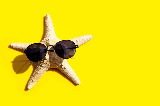 Étoile de mer avec des lunettes de soleil sur fond jaune. Profitez du concept de vacances d'été. Espace de copie - Photo, image