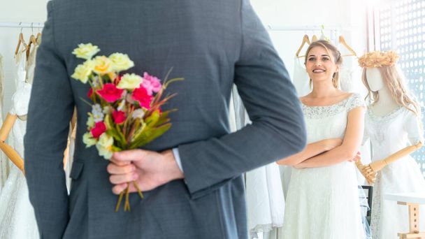 ein Paar steht gerne im Hochzeitsstudio mit einem Mann Überraschung geben Blumenstrauß aus seiner Hand an die Braut. - Foto, Bild