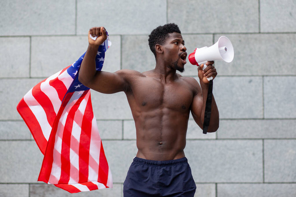 L'uomo afroamericano con la bandiera degli Stati Uniti grida in un megafono e protesta sullo sfondo della città, le vite nere contano il concetto - Foto, immagini