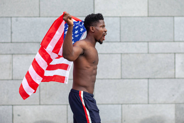 アフリカ系アメリカ人の男性でアメリカ国旗の抗議と叫びが路上での侵略を示していますストライキ中の活動家男性黒人の生活問題の概念 - 写真・画像