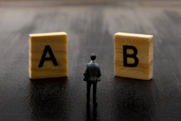 Miniatűr figura, mint üzletember, aki döntést hoz az A és B megoldásról, minimalista absztrakt kép. - Fotó, kép