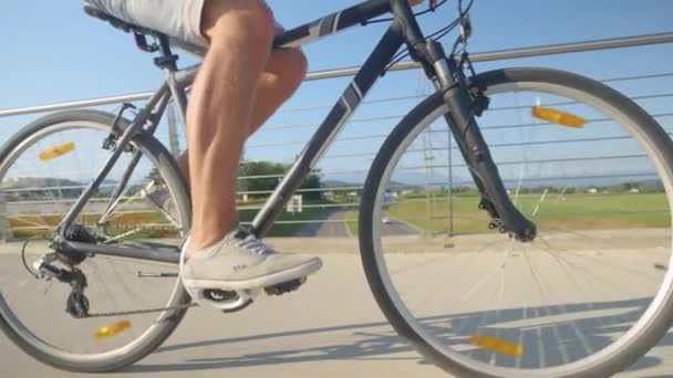 CLOSE UP: Unrecognizable man in jean shorts pedals a bicycle across a bridge. - Footage, Video
