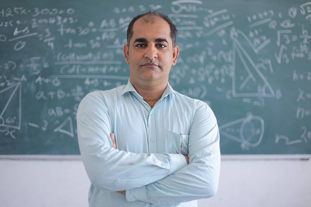 Portret van een serieuze mannelijke leraar die zich verzet tegen schoolbordonderwijs in wiskunde in klaslokaal, school en onderwijsconcept. - Foto, afbeelding