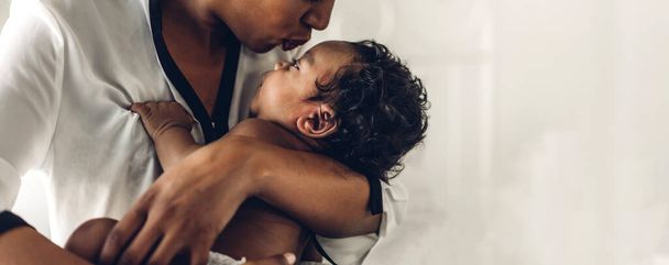 幸せな愛の家族の肖像画アフリカ系アメリカ人の母親は愛らしい小さなアフリカ系アメリカ人の赤ちゃんと遊んでいます.お母さんは白い寝室で楽しい時間をかわいい息子の瞬間に触れて.ブラック家族の概念の愛 - 写真・画像