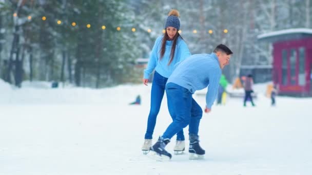 joven hombre patina alrededor de chica y se cae en pista de hielo
 - Metraje, vídeo