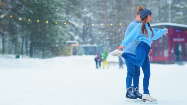 girl in hat skates around happy guy on outdoor ice rink - Footage, Video
