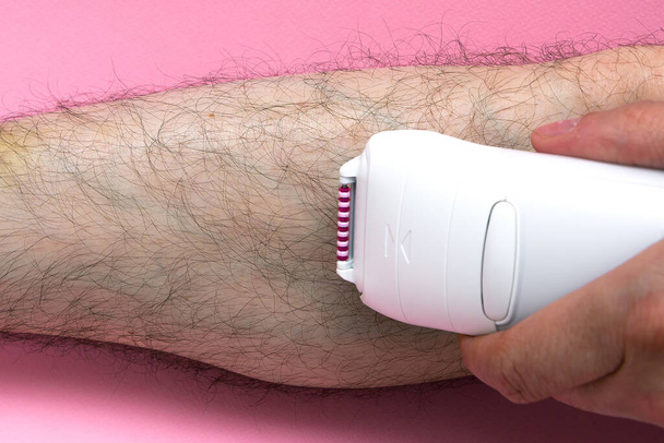 Man epilates his leg with an electric epilator device. close-up male fragment leg shaver shaving. Skin Care and Health. Hair Removal. - Zdjęcie, obraz