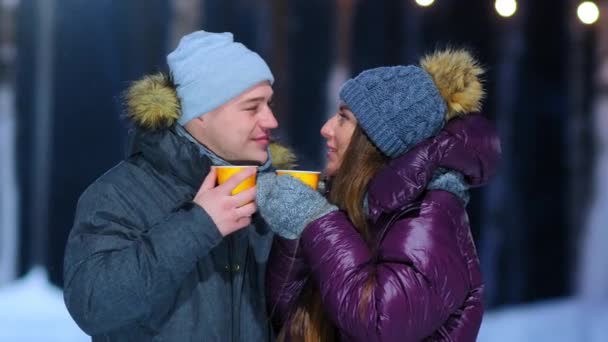 facet i dziewczyna w ciepłe kurtki trzymać filiżanki gorących napojów na lodowisku - Materiał filmowy, wideo