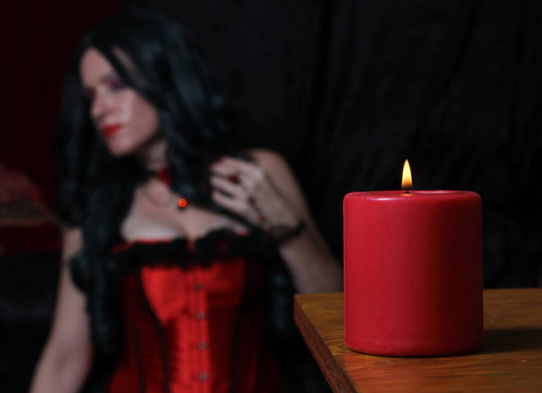 Красная свеча с женщиной в красном корсете на заднем плане
 - Фото, изображение