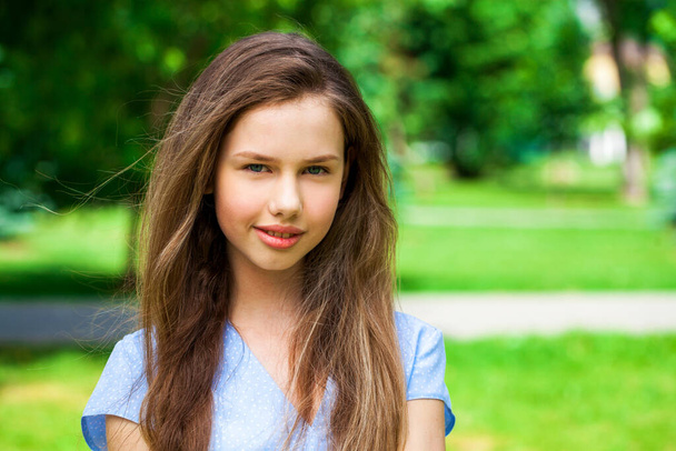 Portrait of a young beautiful brunette girl in blue dress posing in summer park - Photo, Image