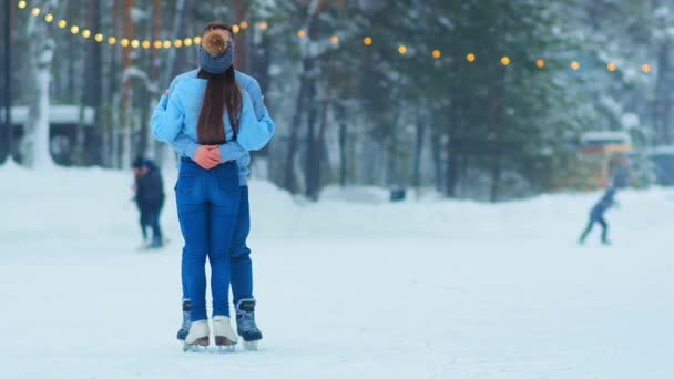 pareja abrazos de pie en pista de patinaje al aire libre con guirnaldas
 - Metraje, vídeo