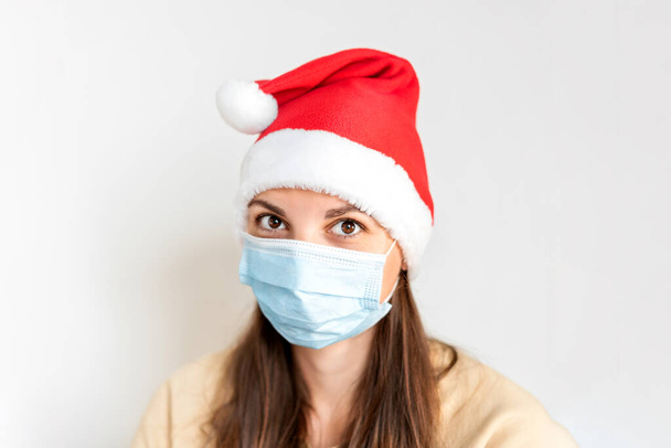 Caucasian sad woman with medical mask and Santa hat. Christmas alone on quarantine - Foto, afbeelding