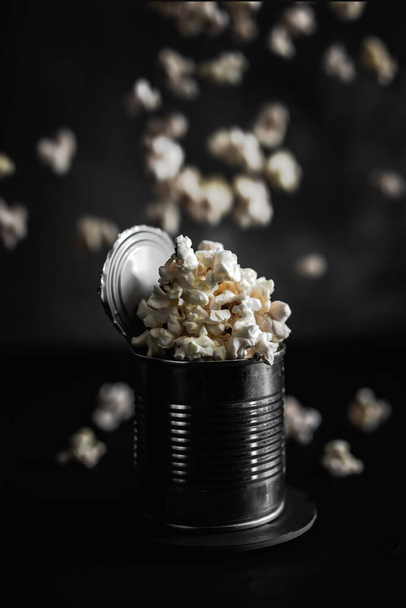 Popcorn in a steel tin, falling popcorn on dark background, moody photo - Fotó, kép