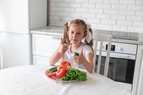 little girl eats vegetables in the kitchen. vegetarianism. child eats plant food. Copy space - 写真・画像