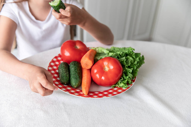 little girl eats vegetables in the kitchen. healthy food. vegetarianism. child eats plant food - Foto, Imagem