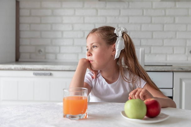 little girl with juice and fruit apples in the kitchen. healthy food. vegetarianism. the child eats plant food. vitamins - Фото, изображение