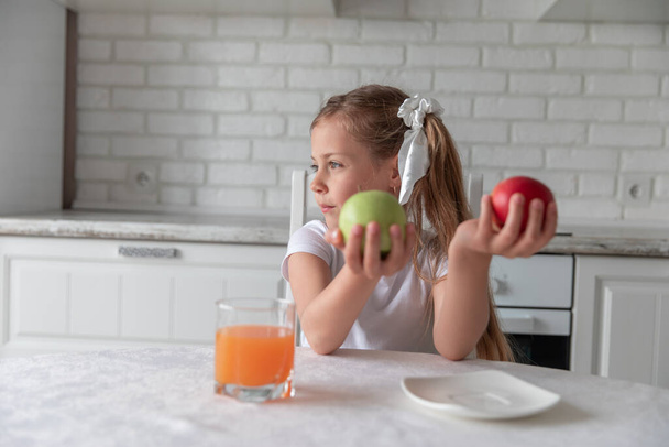 little girl with juice and fruit apples in the kitchen. vegetarianism. the child eats plant food. vitamins - Foto, imagen