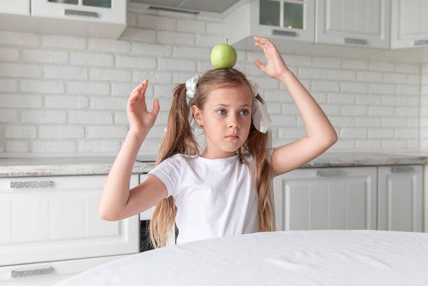 little girl with apple on her head in the kitchen. new idea. Copy space. - Zdjęcie, obraz