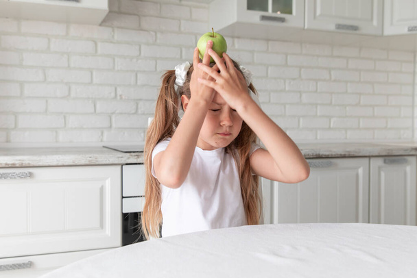 little girl with apple on her head in the kitchen. new idea. Copy space. - Фото, изображение