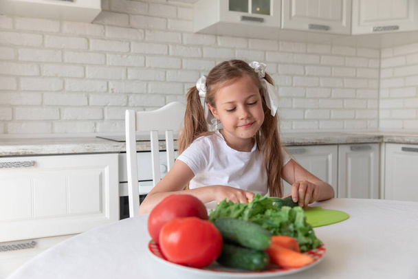 little girl in the kitchen cutting vegetables. vegetarianism - Fotó, kép