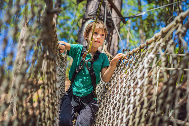 Portrait of cute little boy walk on a rope bridge in an adventure rope park - 写真・画像