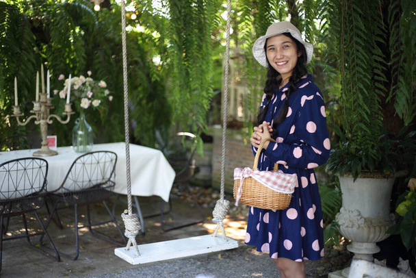 Frau hält einen Korb neben einer Schaukel im Garten - Foto, Bild