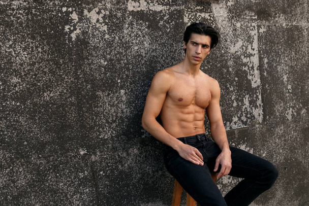 Porträt eines sexy männlichen kaukasischen Models mit muskulösem Körper, das an einer alten schwarzen Wand posiert. Männergesundheit. - Foto, Bild