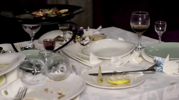 Assiettes sales avec restes, bouteilles et verres éparpillés sur la table après le banquet. - Séquence, vidéo