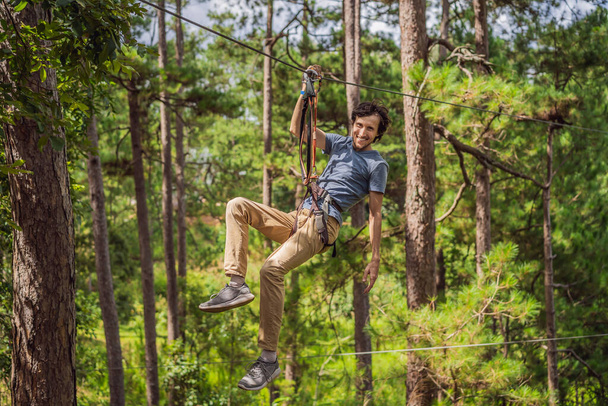 Young attractive man in adventure rope park in safety equipment - Фото, изображение