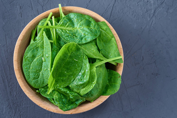 Fresh spinach leaves in wooden bowl on a dark background. Organic food - Photo, image
