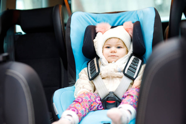 Urocza dziewczynka z niebieskimi oczami siedząca w foteliku samochodowym. Dziecko w zimowych ciuchach jedzie na rodzinne wakacje i do Jorneya. Bezpieczna podróż, bezpieczeństwo dzieci, koncepcja transportu. - Zdjęcie, obraz