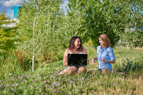 Two happy girlfriends work with a laptop in the park - Fotoğraf, Görsel