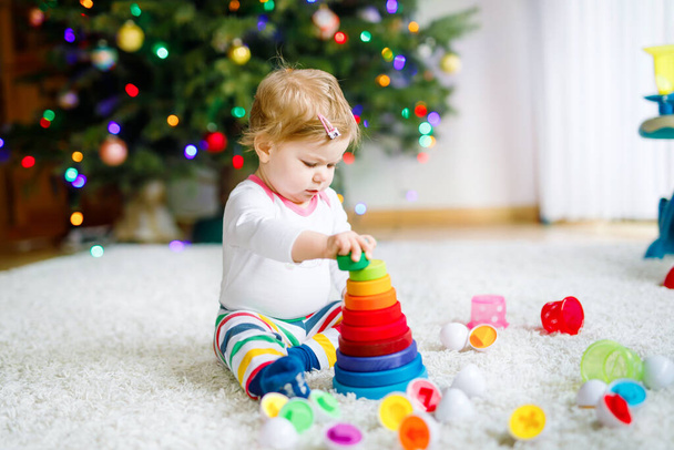 Adorable cute beautiful little baby girl playing with educational toys at home or nursery. Happy healthy child having fun with colorful wooden rainboy toy pyramid. Kid learning different skills. - Photo, Image