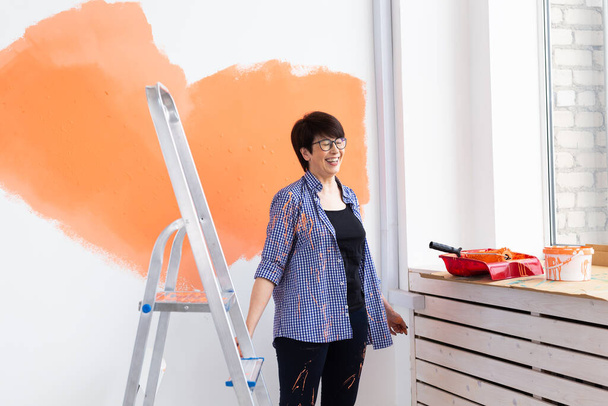 Αρκετά μεσήλικη γυναίκα με ρολό ζωγραφικής σε εσωτερικούς χώρους. Ανακαίνιση, ανακαίνιση, επισκευή διαμερισμάτων και αναψυκτικό. - Φωτογραφία, εικόνα