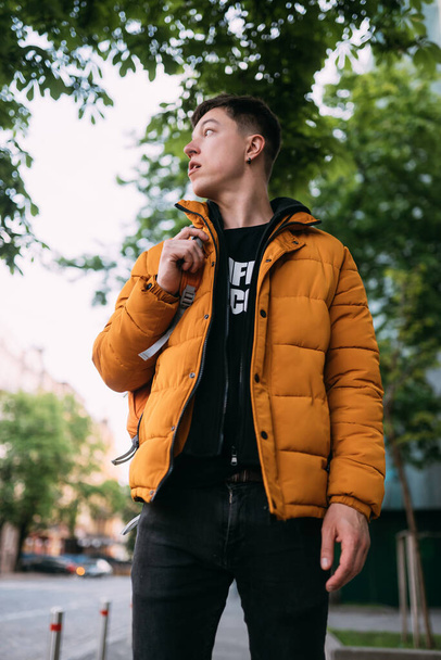 Homem adulto jovem em uma jaqueta amarela e jeans anda em uma rua da cidade
 - Foto, Imagem