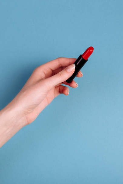 La mano de las mujeres está tomando lápiz labial rojo. aislado En el fondo azul - Foto, Imagen