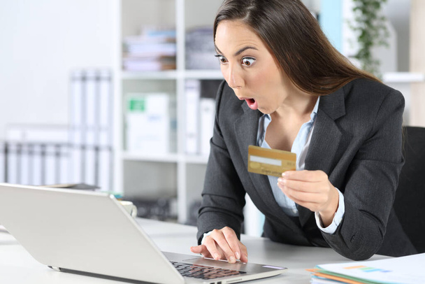 Surprised executive woman pays online with credit card on laptop sitting on a desk at office - Fotografie, Obrázek
